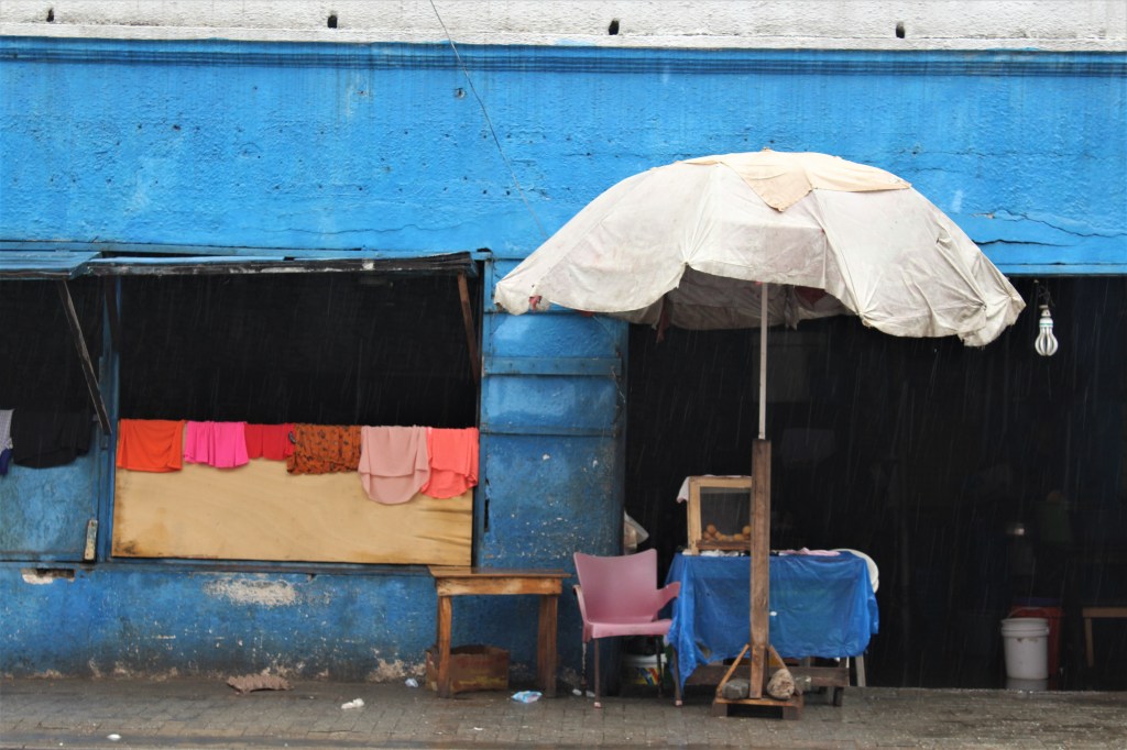 A blue building in old Accra with an umbrella in the front and clothes drying over a wall. 