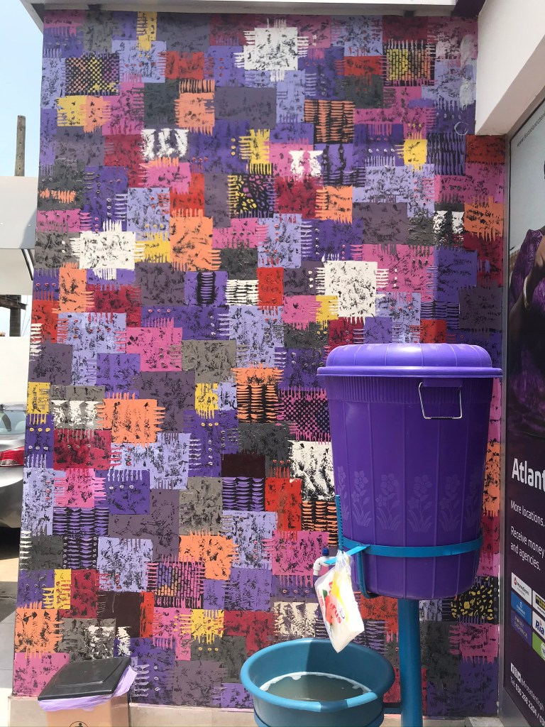 Ghana during the Corona pandemic, A veronica bucket stands in front of a wall painted like traditional Kente cloth