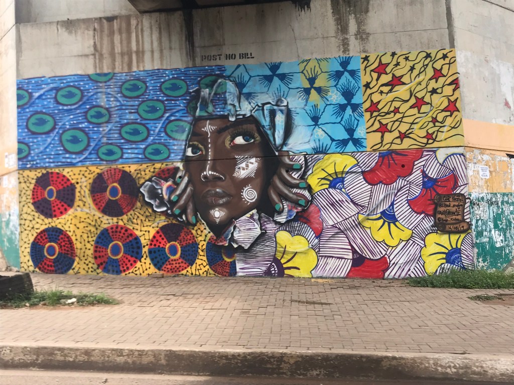 A street mural in Airport area in Accra Ghana of a lady pulling herself through African wax fabric. 