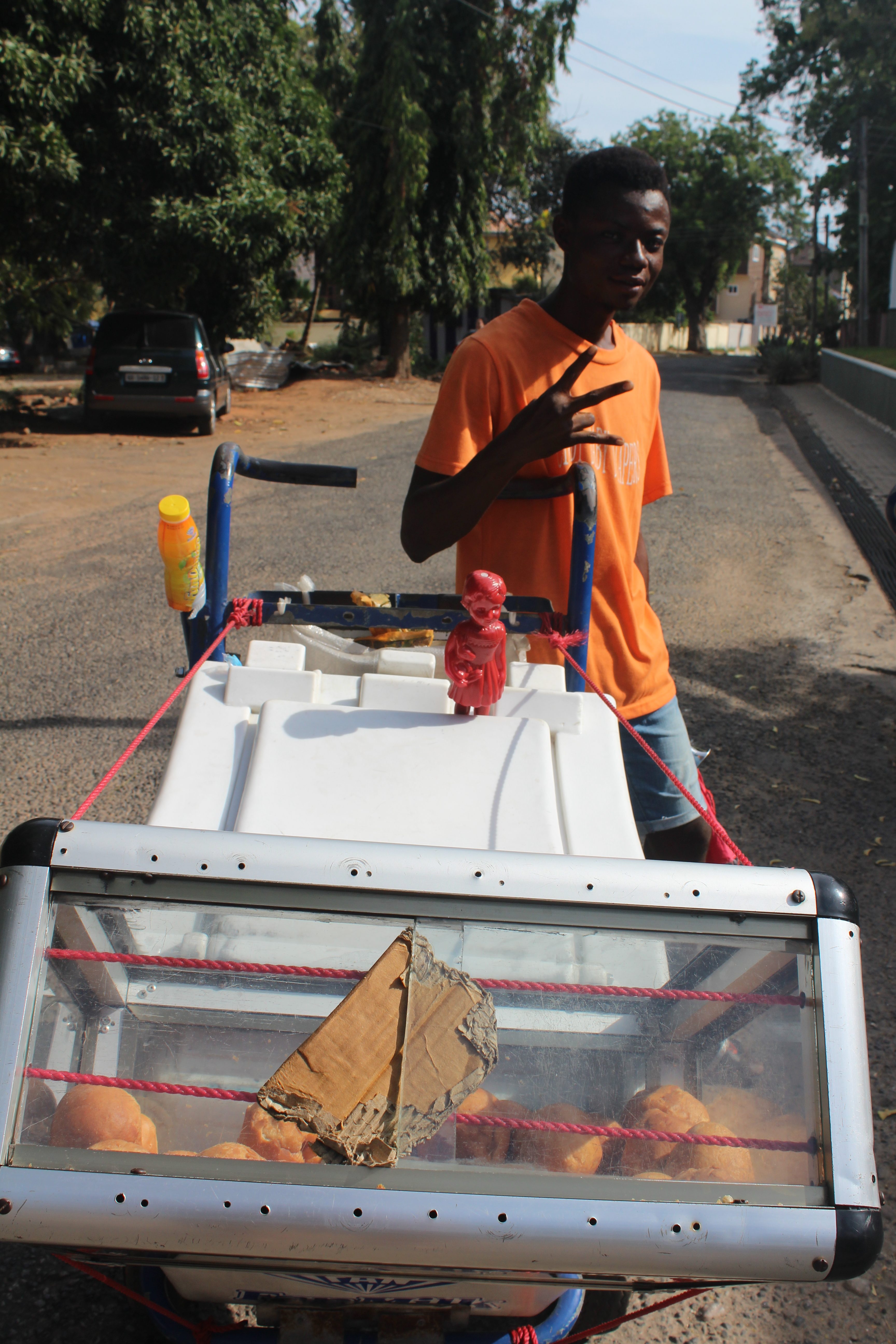 A red Clonette doll stands at the bike of a man selling fried Bofrot in Accra Ghana