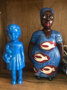 A blue Clonette Doll stands on our bookshelf next to a Ghanaian wooden figure of a woman.