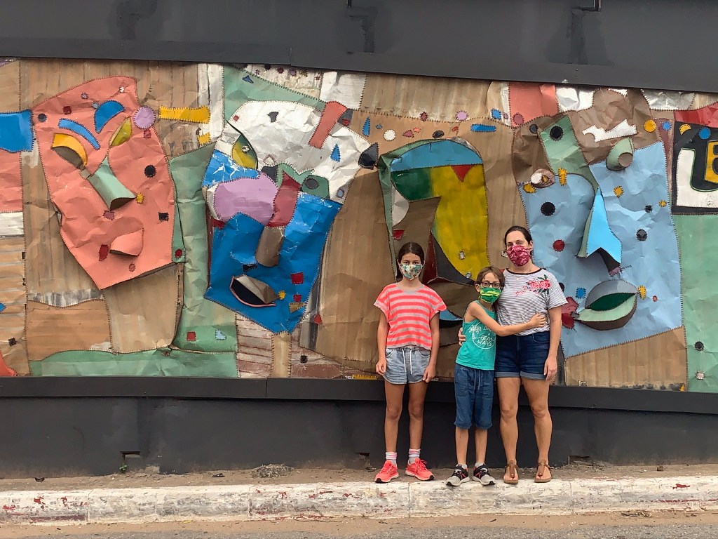Blogger Lauren Simpson stands with her children in front of Ghanaian artist Tei Huagie's metal street artwork in Accra Ghana