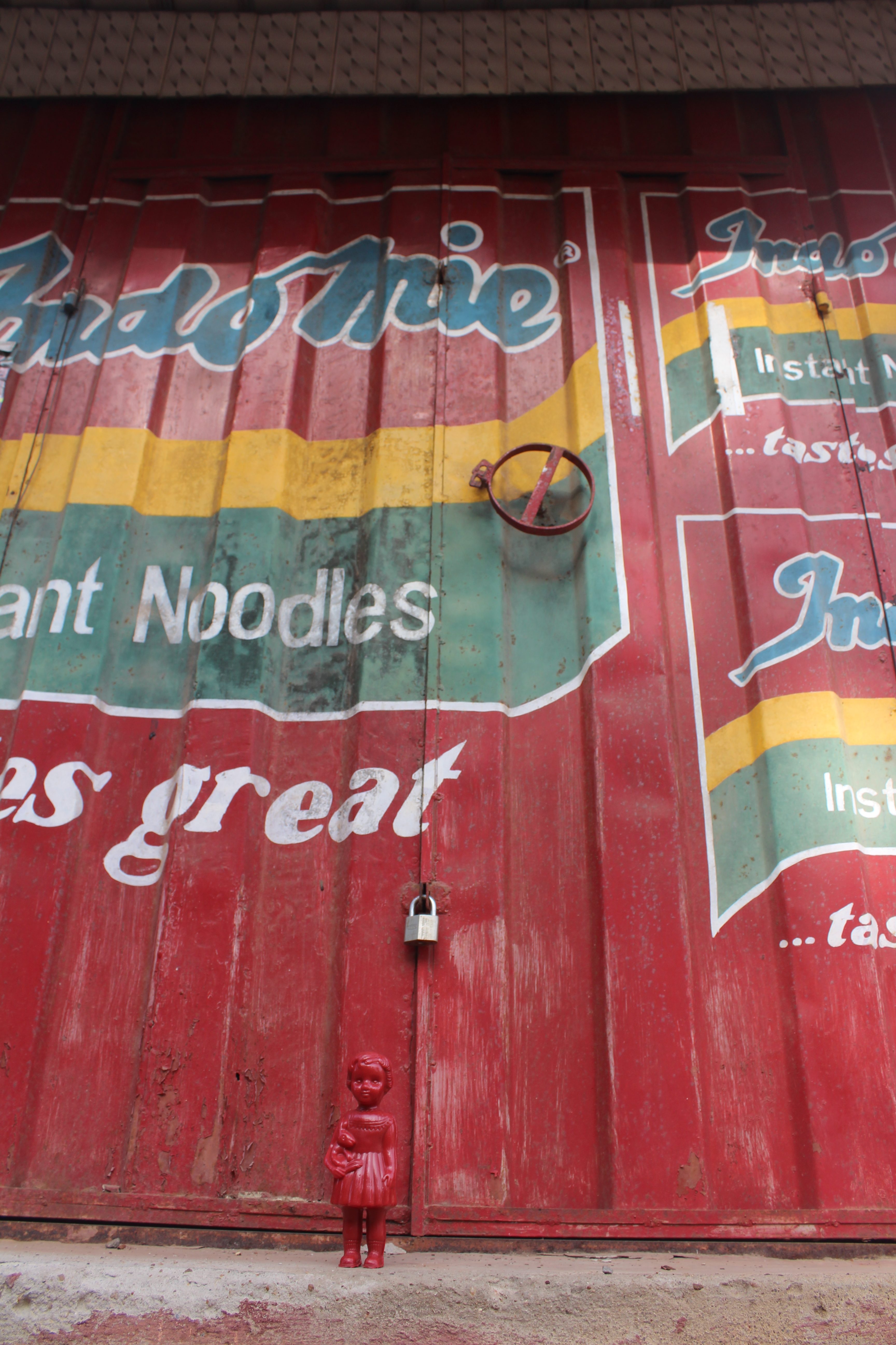 A Red Clonette doll stands in front of a kiosk advertising Indomie instant noodles in Accra Ghana