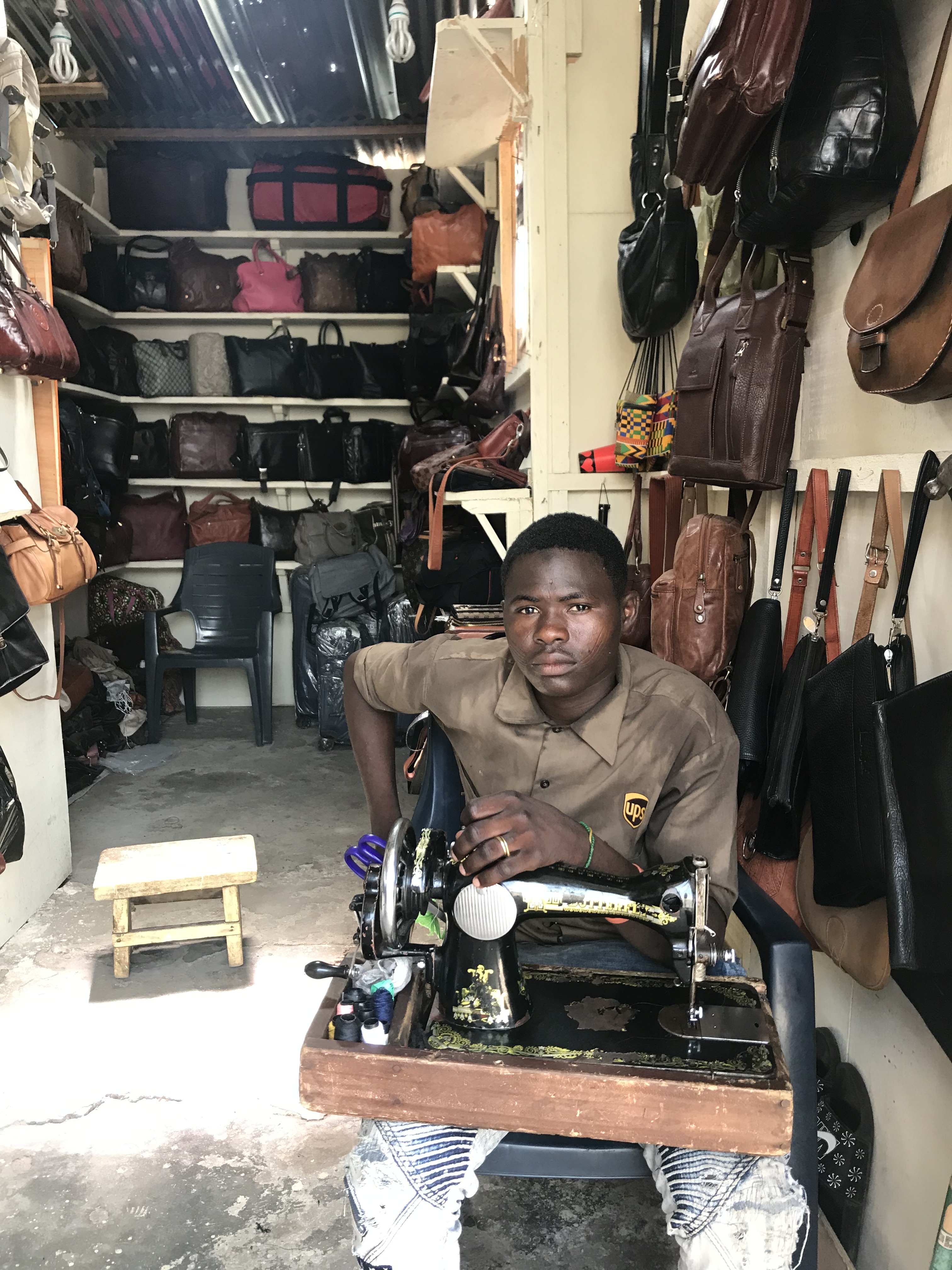 A man who walks around with his sewing machine on Accra's Streets sitting in a shop selling leather handbags on Oxford Street.